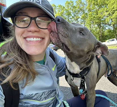 Dog licking the face of a woman sitting outdoors