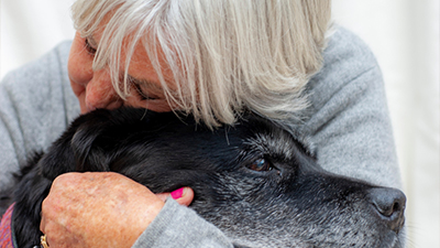Elderly woman hugging elderly black and grey dog